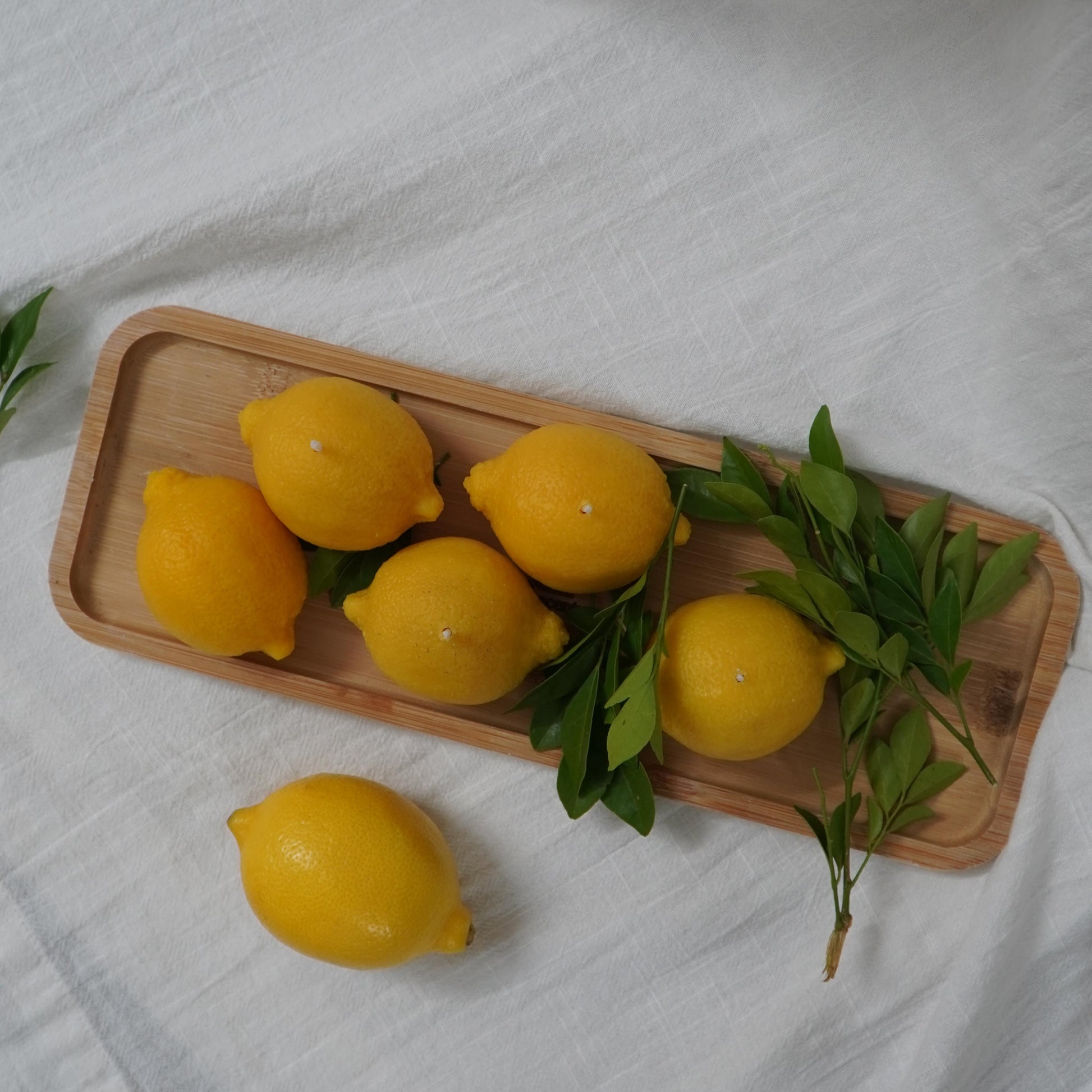 Yellow lemons with green leaves on a wooden tray over a white fabric background
